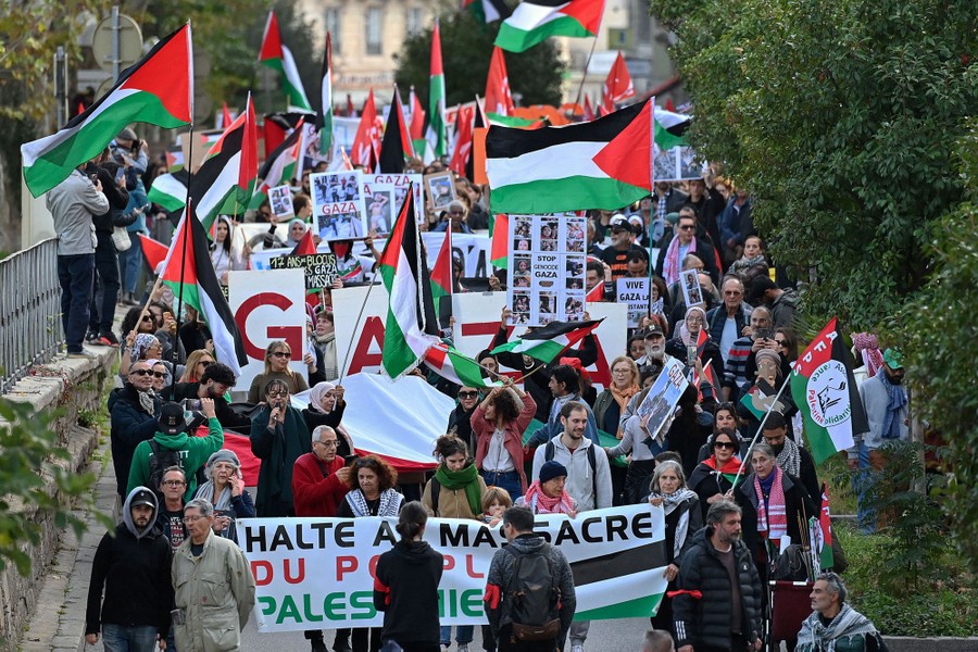 A crowd of protesters walk in a street carrying Palestinian flags.