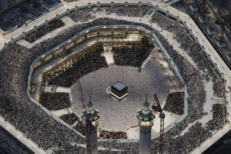 Muslims praying at the Kaaba, arranged in circles on the ground level and in seating in a surrounding structure