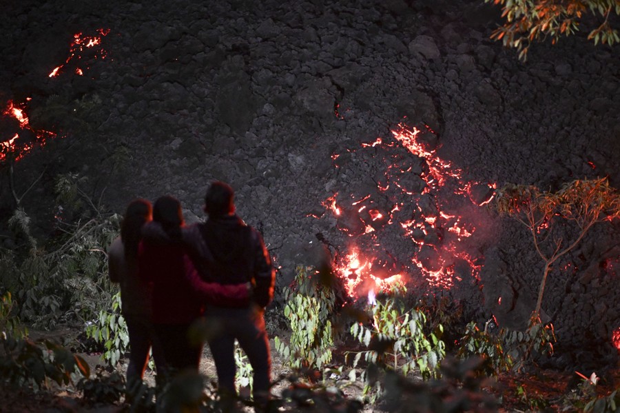 People stand near a slow-moving lava flow at night.