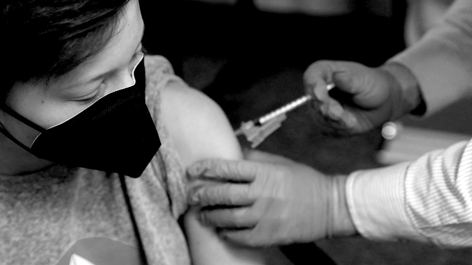 A young person wearing a mask receives a shot in the arm