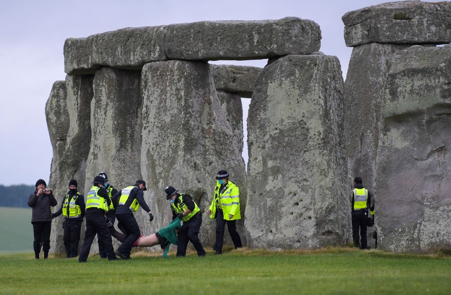 Several police officers carry a person away from Stonehenge.