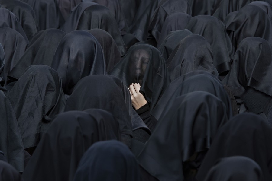 One woman at the center reacts, among a crowd of women wearing black veils.