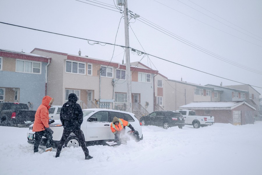 Several people work to free a car stuck in deep snow.