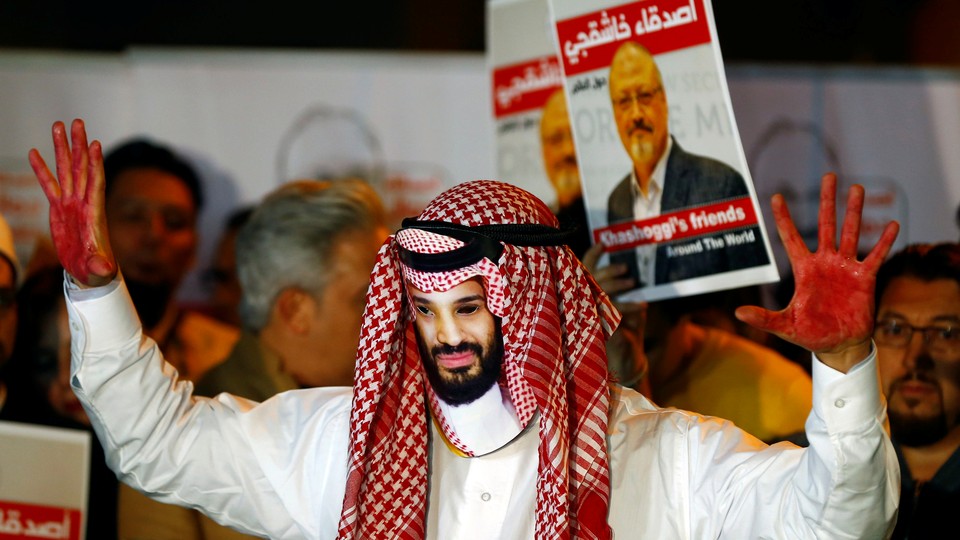 A demonstrator wearing a mask of Saudi Crown Prince Mohammed bin Salman attends a protest outside the Saudi consulate. In the background, other demonstrators hold signs with pictures of Jamal Khashoggi.