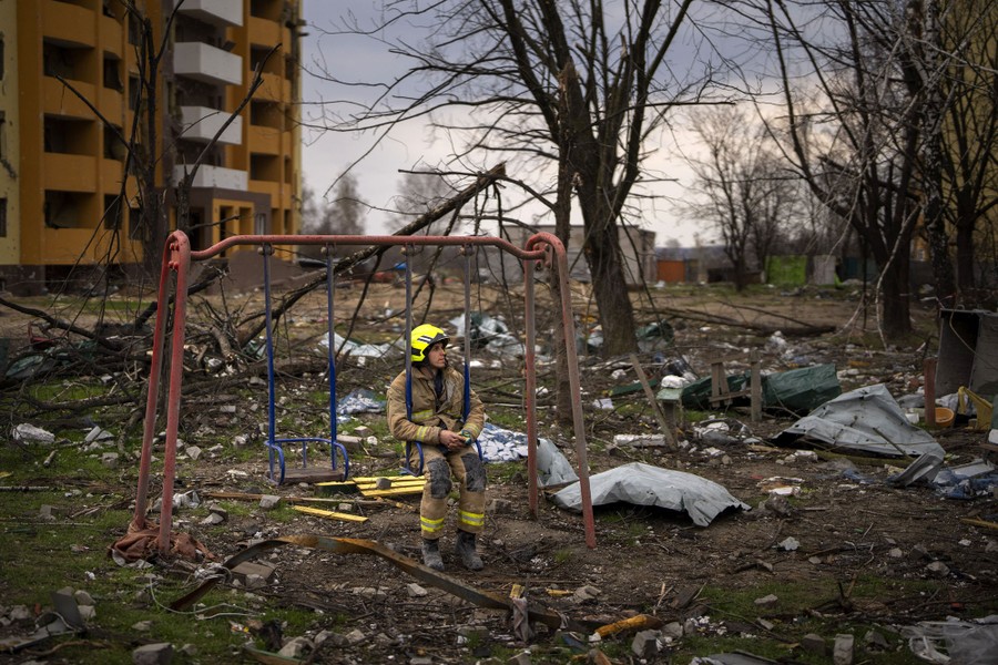 A firefighter sits on a swing amid debris, next to a destroyed building.