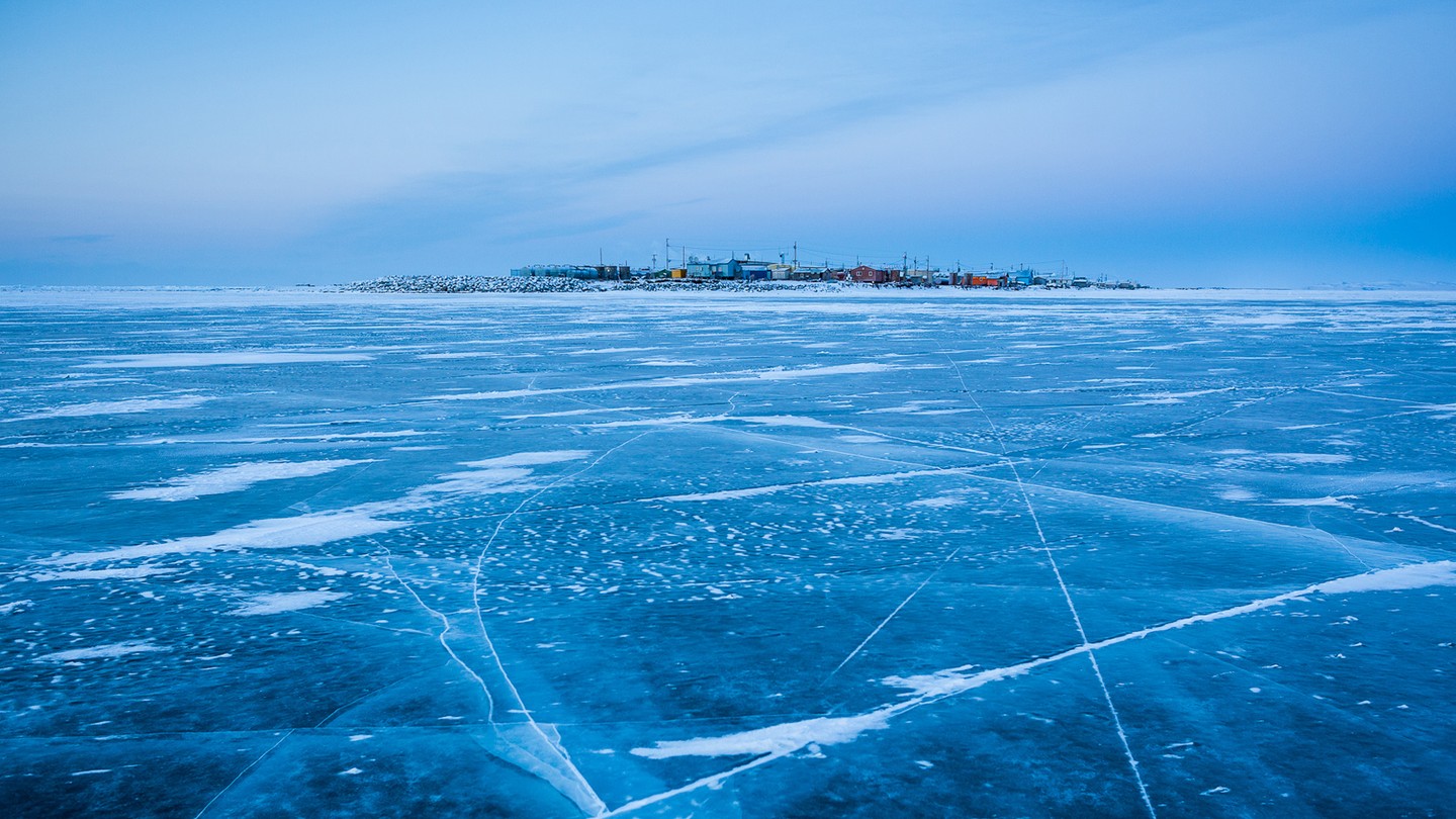 A frozen over body of water, with scratches and white patches on the ice