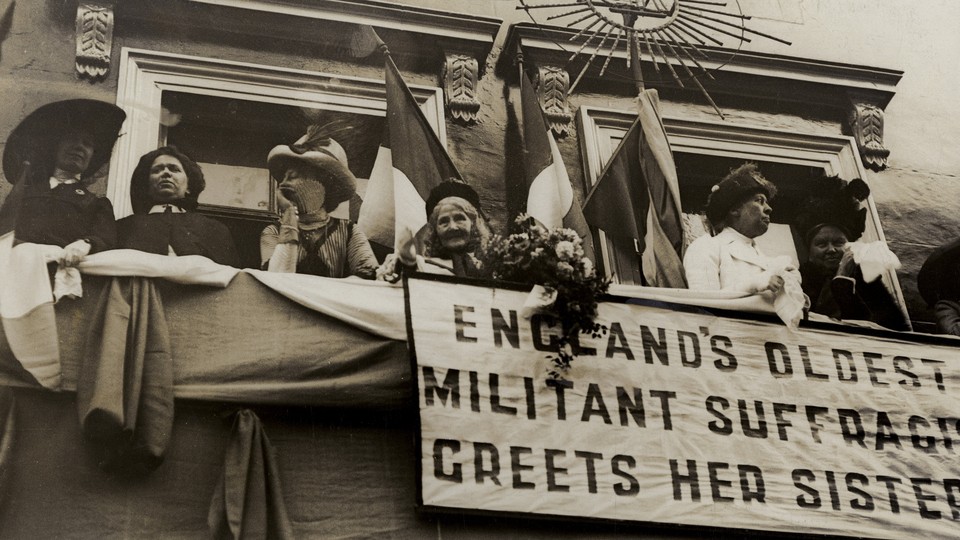 Elizabeth Wolstenholme Elmy by a banner that reads "England's Oldest Militant Suffragist Greets Her Sisters"