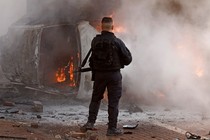 A member of the Israeli security forces next to a burning car