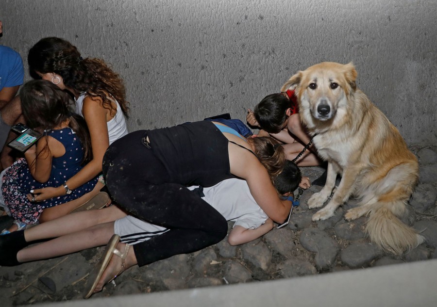 Several people and a dog take cover, getting low beside a concrete wall.
