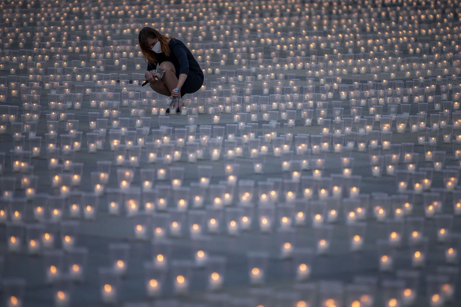 A woman kneels down to light a candle among thousands of other candles arranged in a courtyard.