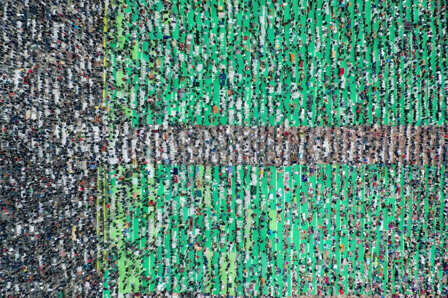 An aerial view of a large crowd of people standing in lines and praying