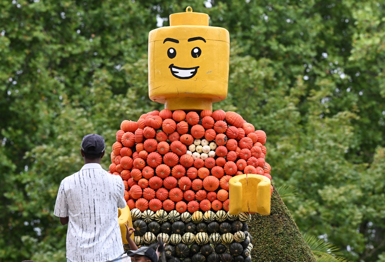 People look at a tall figure of a Lego man made of pumpkins.