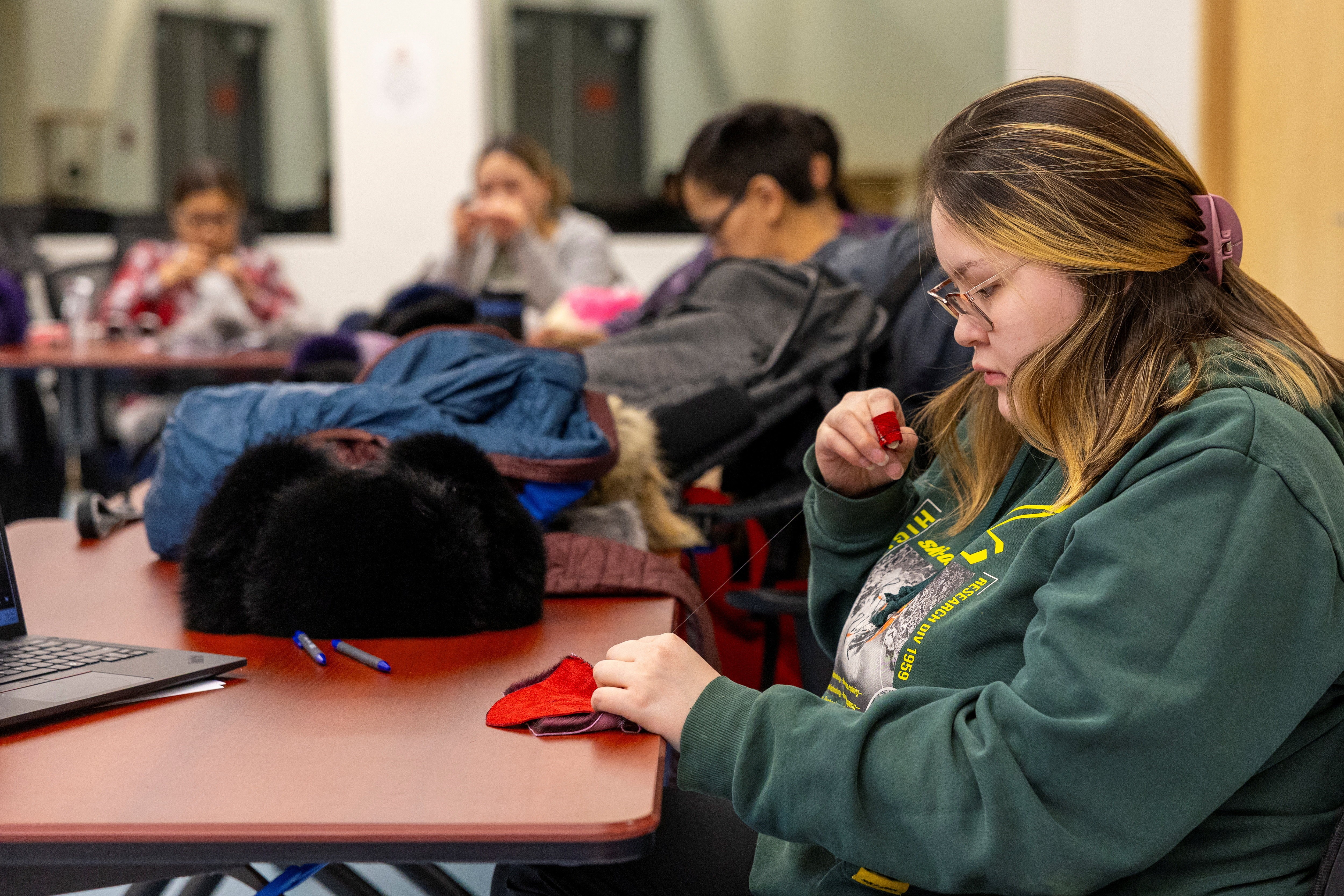 Several people sit in a classroom, working on sewing projects.