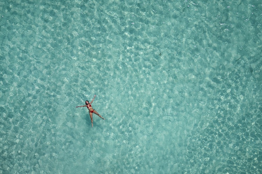 An aerial view of a swimmer floating in clear blue-green water.