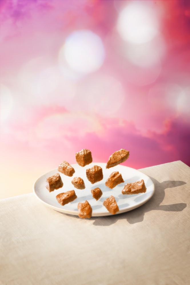 Picture of a few pieces of meat floating above a plate with a pink background behind it