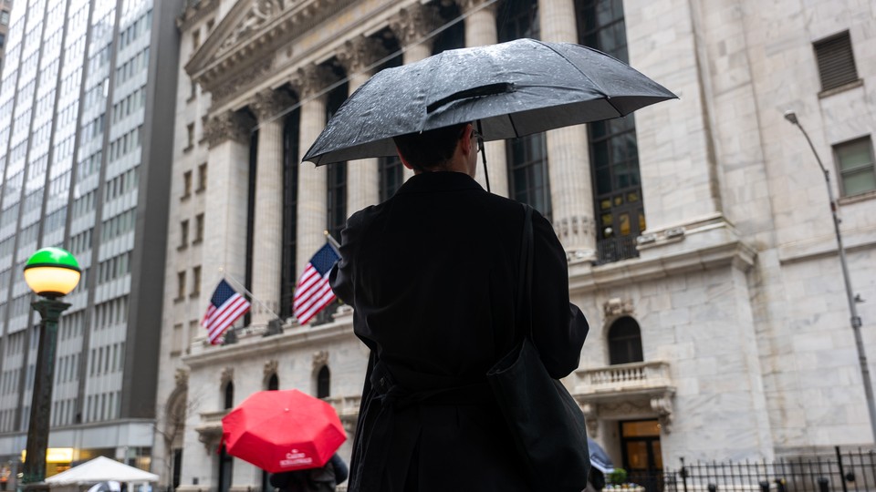 Photo of man standing with an umbrella outside the New York Stock Exchange