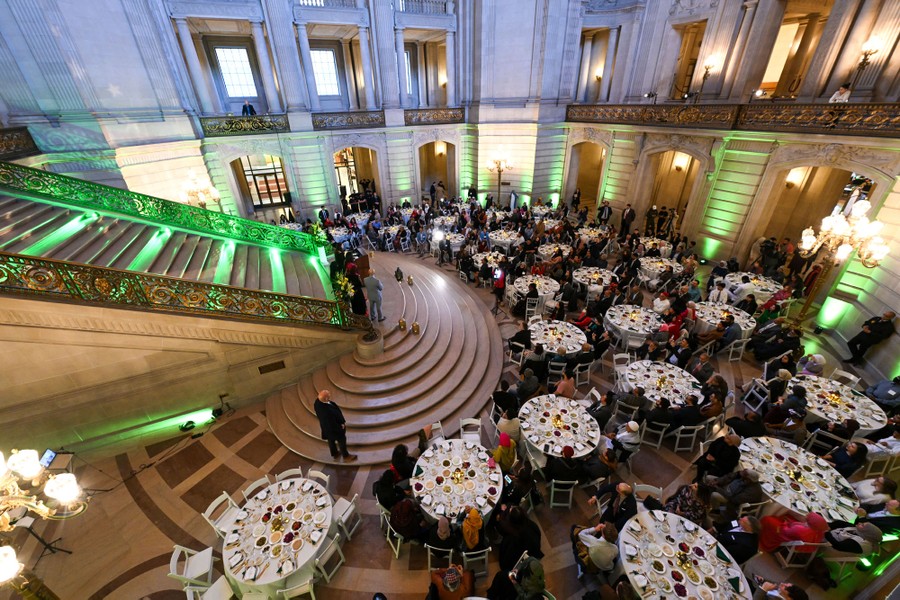 Δεκάδες μεγάλα τραπέζια είναι τακτοποιημένα για ένα κοινό γεύμα μέσα σε ένα κτίριο του δημαρχείου.