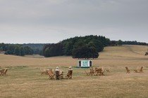 Two women sitting in chairs talking to each other in the midst of a wide open field at what looks like a concert venue