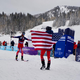 Cam Smith approaches Anna Gibson at the finish line of a ski mountaineering race, both with arms outstretched, Gibson with the American flag across her shoulders