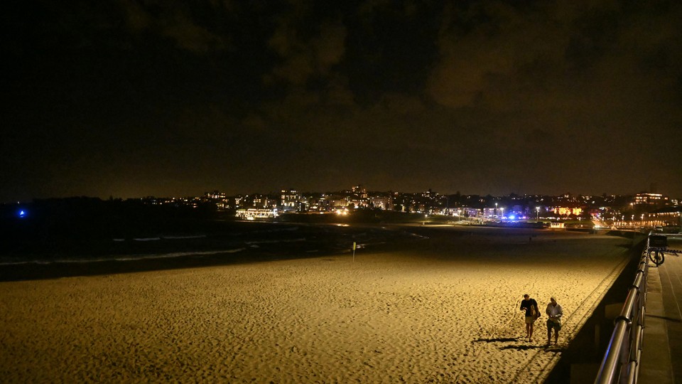 Photograph of a deserted Bondi Beach at night with two people walking on the sand