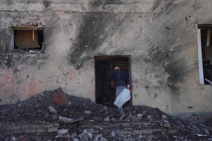 A person walks through a doorway in a heavily-damaged building's wall.