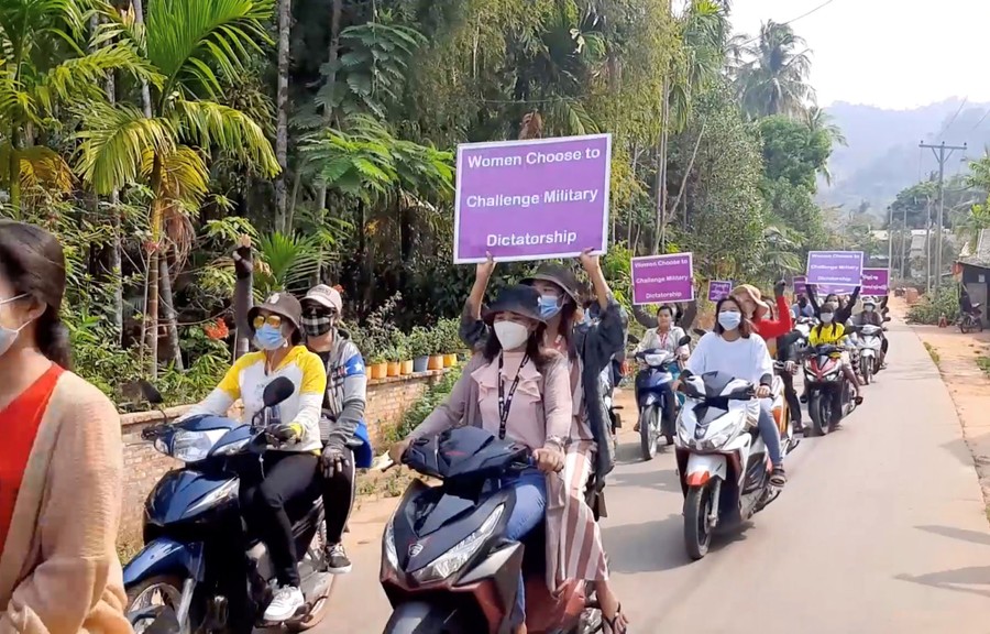 Dozens of people ride motorcycles together, many holding up signs that read "Women choose to challenge military dictatorship."