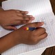 A child holds a pencil and writes on a sheet of notebook paper. 