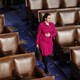 Elise Stefanik wears a pink suit and walks in front of empty seats in the House Chamber
