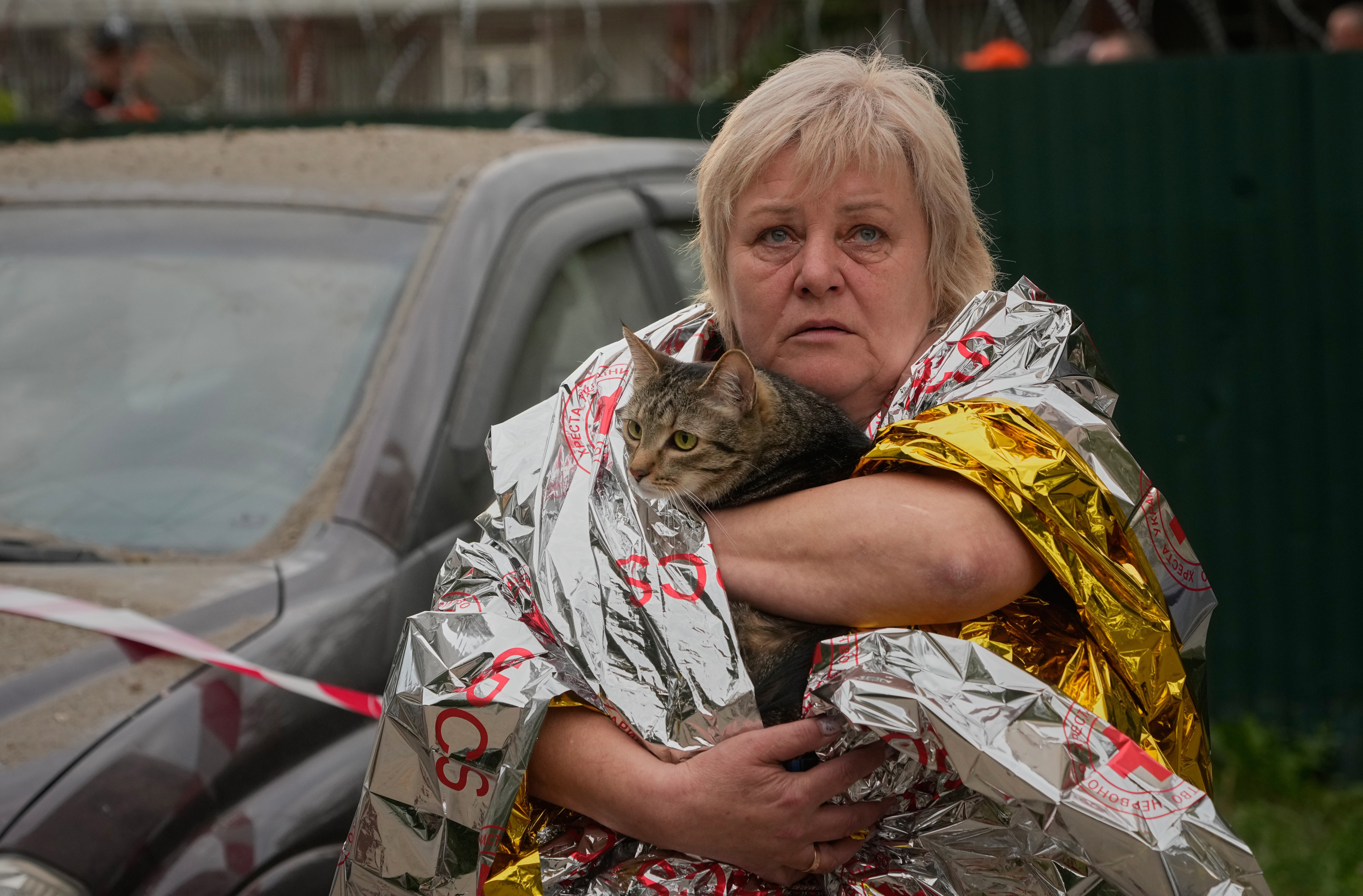 A woman, wearing a shiny emergency blanket, carries a cat to safety.