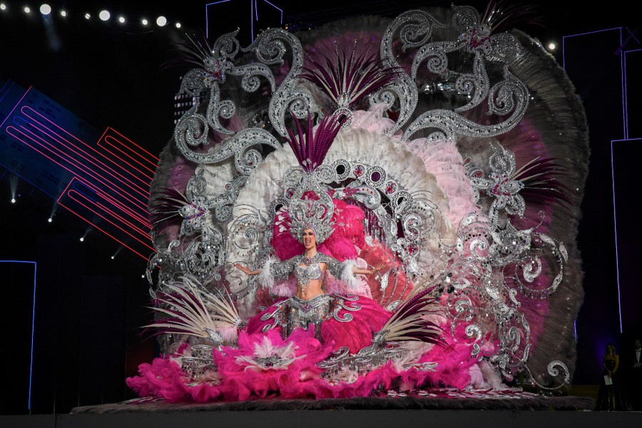 A person performs onstage wearing a huge, elaborate dress that extends a dozen feet above and to the sides of them.