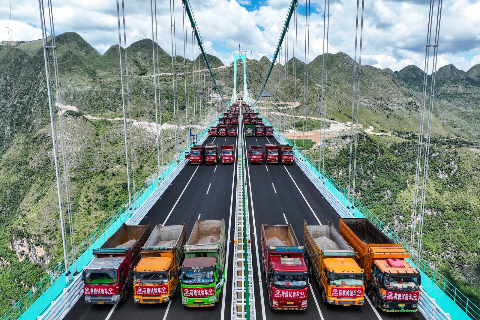 Dozens of dump trucks are seen parked in rows on a brand new road bridge.