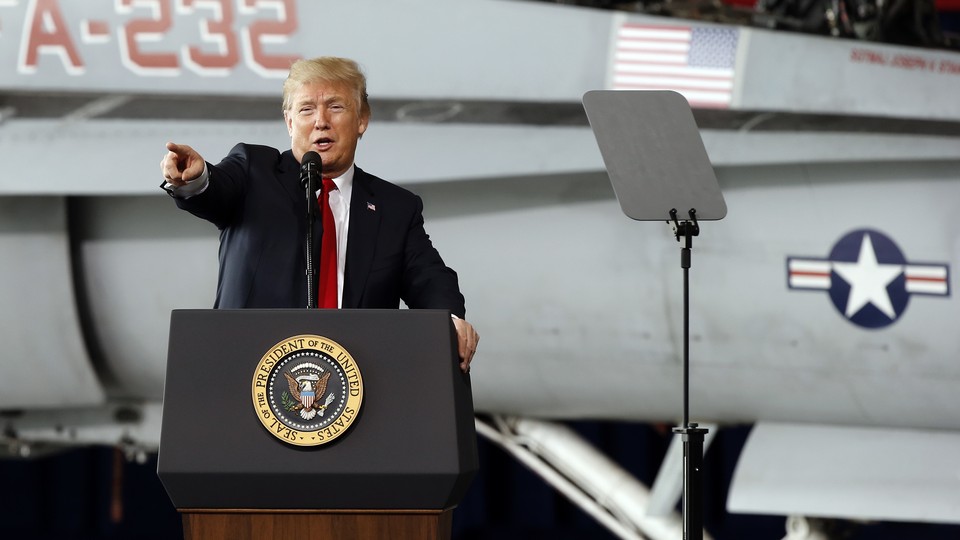 President Trump stands at a podium and points in front of a military airplane.