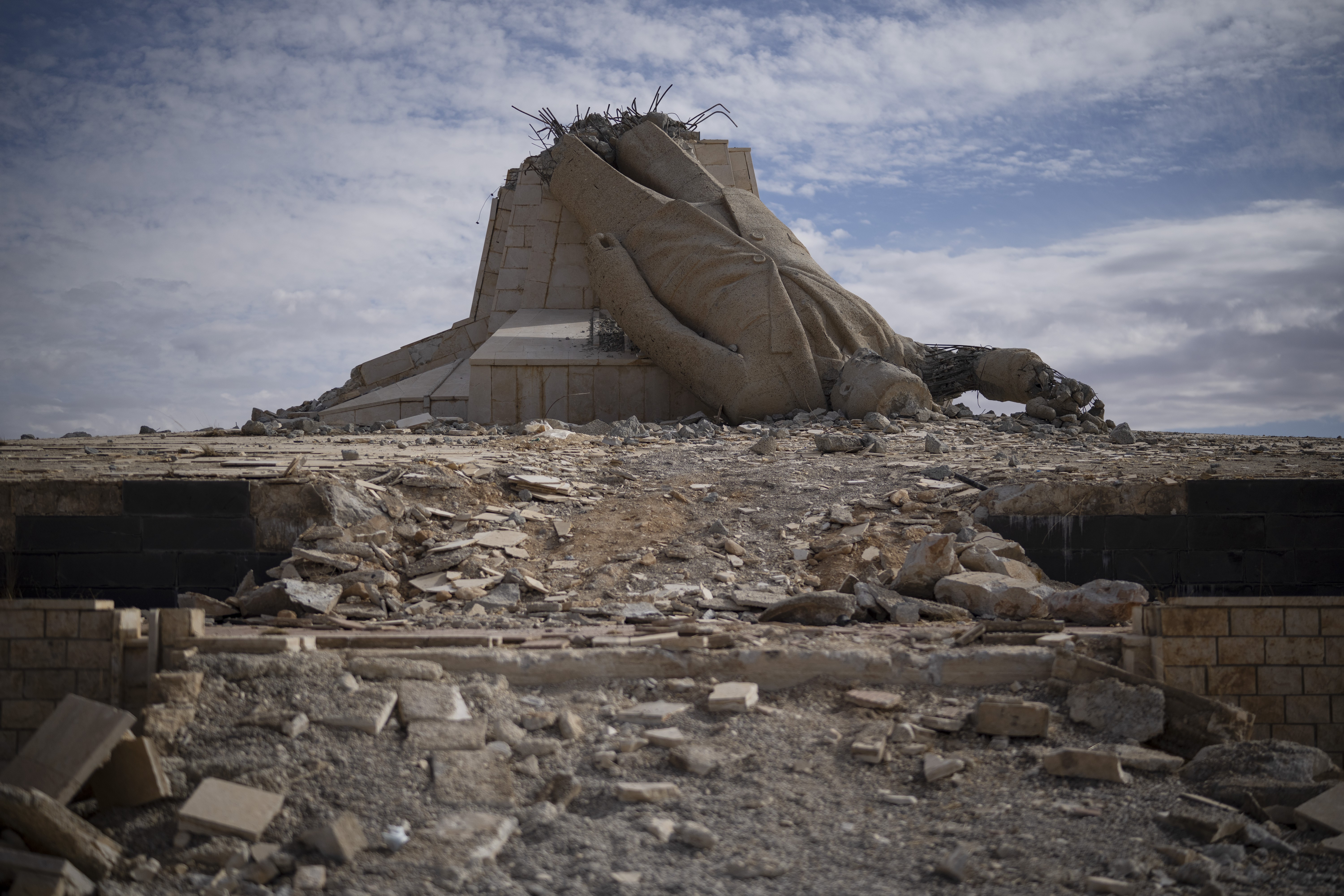 A toppled statue of Hafez Assad lies among piles of debris.