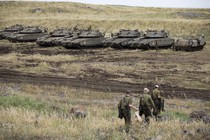 Three soldiers walking in front of a line of tanks