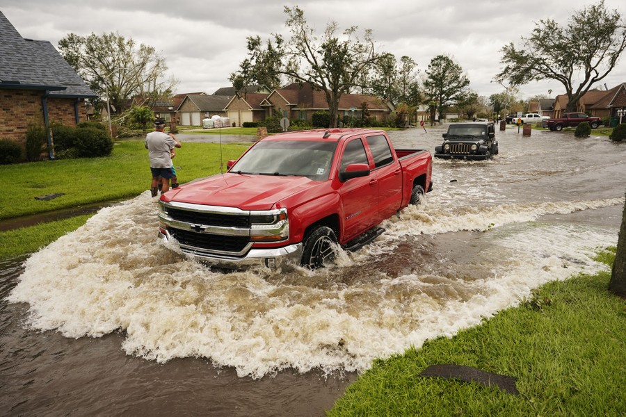 A pickup truck and jeep drive through a flooded street causing waves.