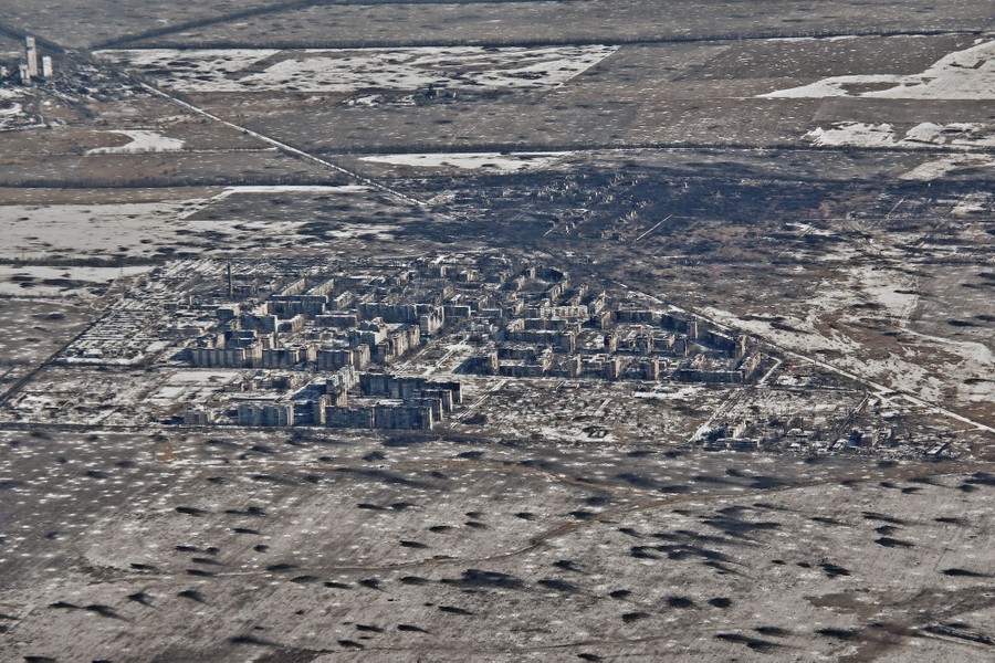 An aerial view of a heavily-damaged town, surrounded by open fields that are pock-marked by craters and blast marks.
