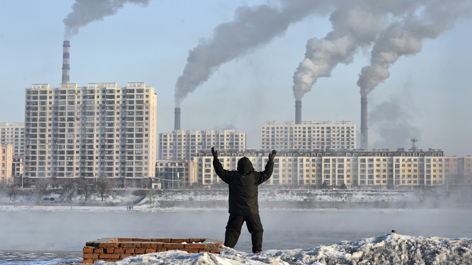 A photograph of a person facing away from the camera, standing with their arms raised, in front of factories with smokestacks emitting smoke