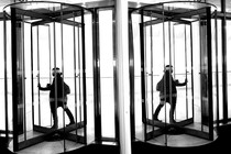 A woman walks through an office's revolving door next to a mirrored wall.