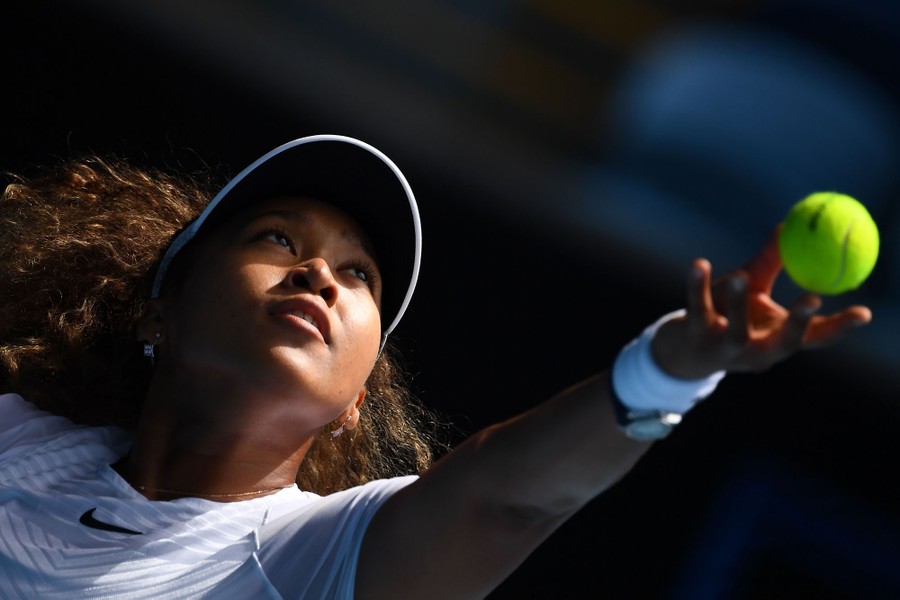 Naomi Osaka tosses a tennis ball as she prepares to serve it.