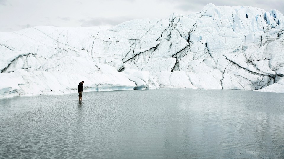 A person stands in water in front of a glacier.