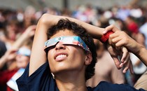 A person wearing eclipse glasses stares up at the sky.
