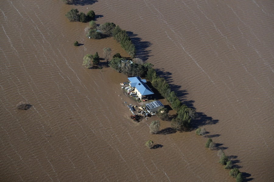 An aerial view of a wide, flooded plain, with a stranded house in front of a stand of trees.