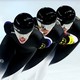 Three speed skaters race, seen close together wearing identical uniforms and helmets with mirrored visors.
