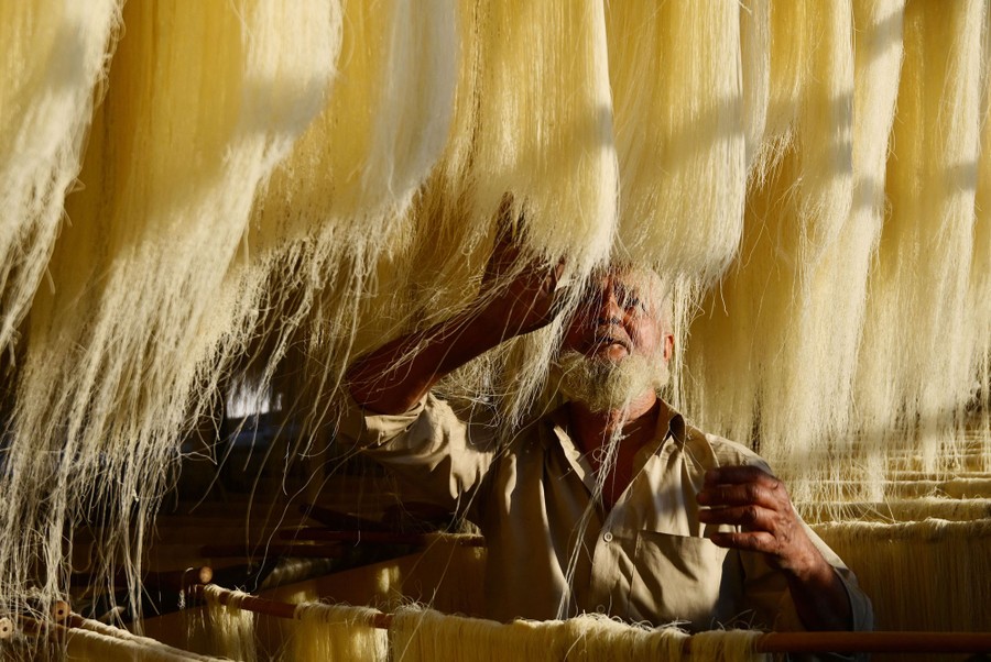 A worker stands beneath racks of drying thin noodles.