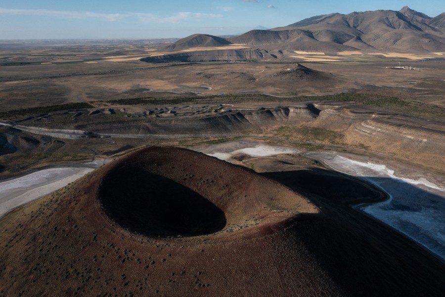 An aerial view of a dry landscape with an ancient volcanic cone in the foreground and a salty basin below it.