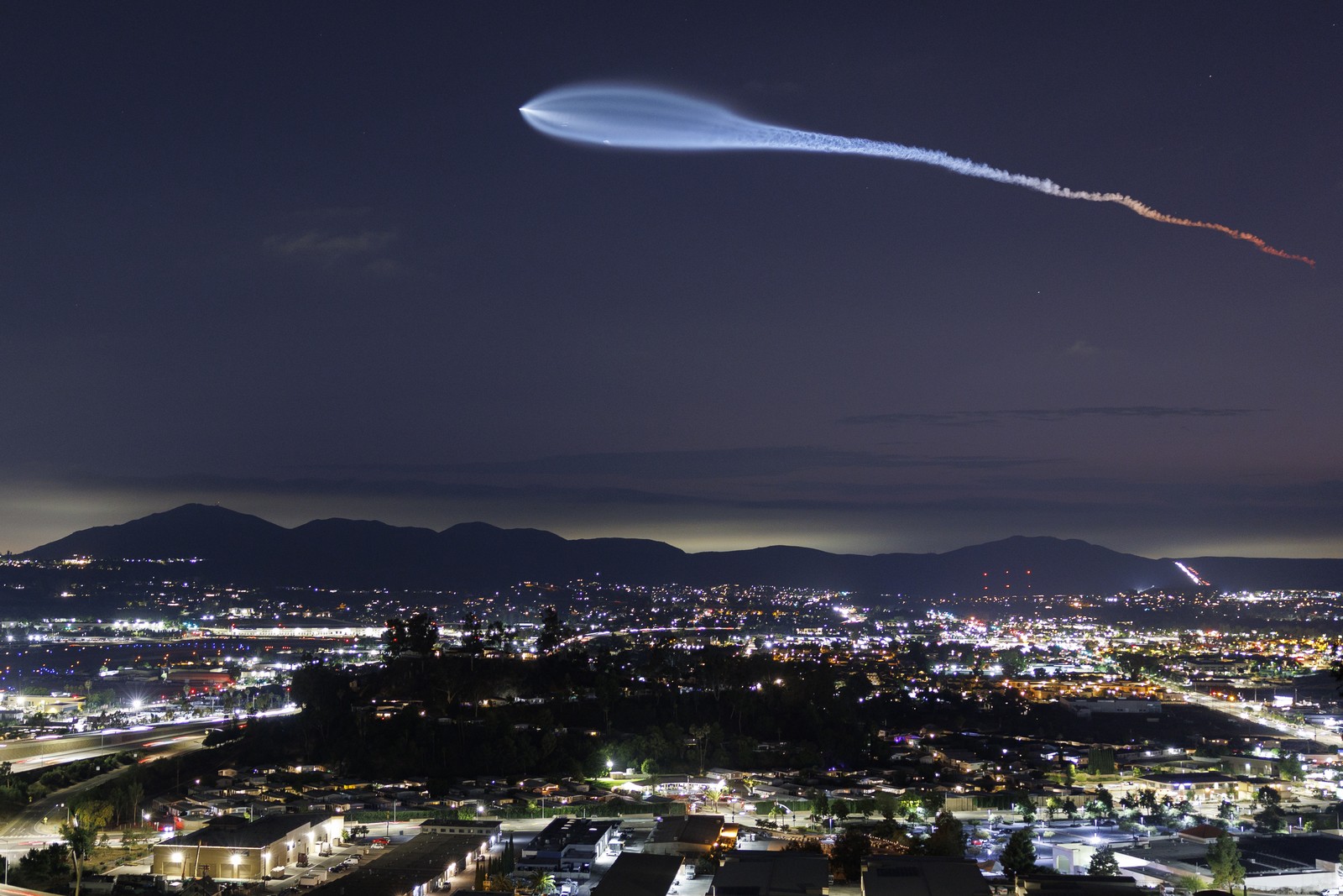 A bright cloud streaks through the night sky following a rocket launch.