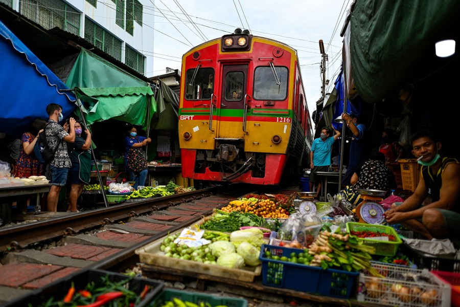 A train rolls through a marketplace, with vendors set up right against the tracks on either side.