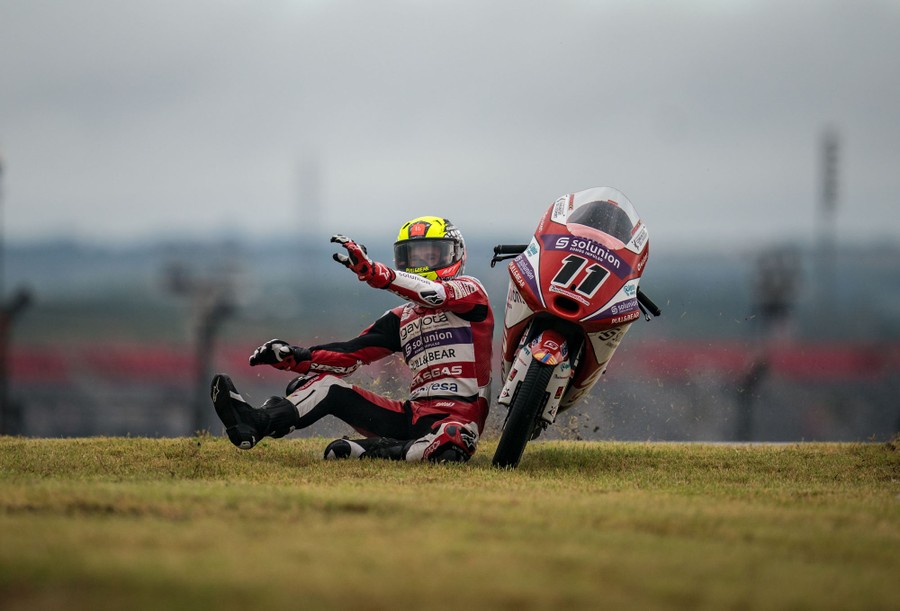 A motorcycle rider falls from his racing bike onto grass.