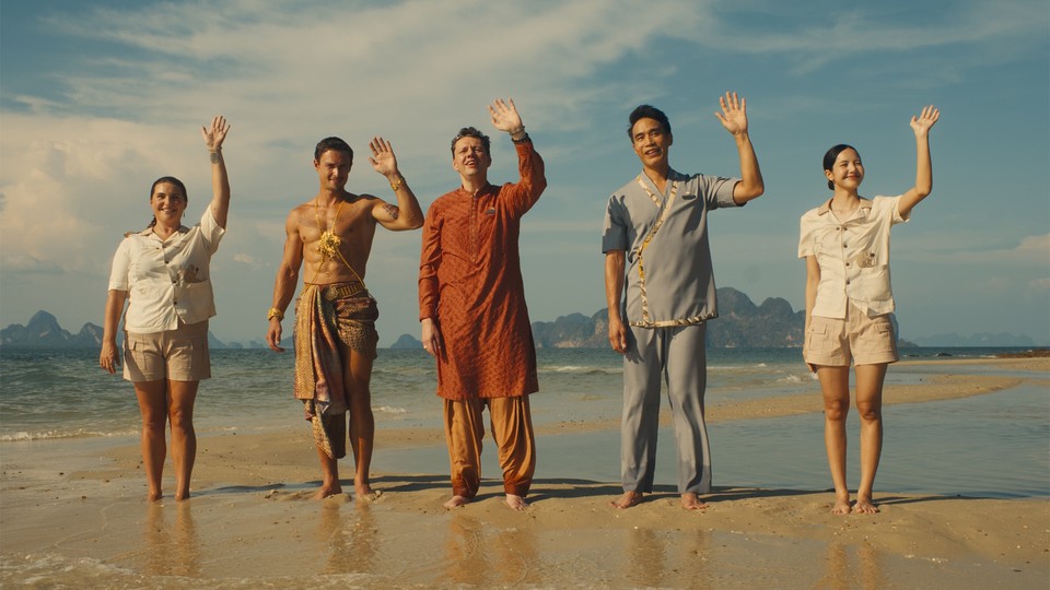 Five people stand waving on a beach
