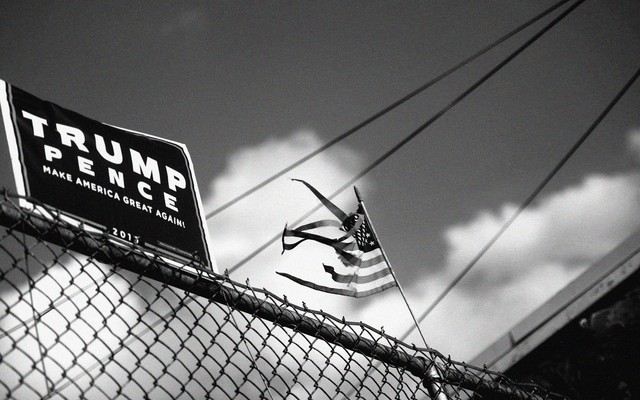 A Trump-Pence campaign sign on a fence with an American flag in the background